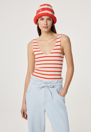 Frau trägt ein rot-weiß gestreiftes ärmelloses Oberteil, hellblaue, hochgeschnittene Hose mit Bindegürtel und gehäkelten rot-weißen Anglerhut.