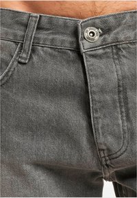 Jeans de denim gris con cierre de botones, bolsillos frontales y costuras en contraste. La tela tiene un acabado ligeramente texturizado.