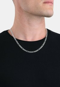 Collana in argento con maglie allungate e interconnesse, che riflettono la luce su uno sfondo di t-shirt nera.