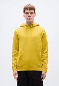 Κίτρινο βαμβακερό φούτερ με τσέπη καγκουρό, ρυθμιζόμενο κορδόνι στο κουκούλι και μικρό τετράγωνο λογότυπο στο στήθος. Λιτή υφή, casual εφαρμογή.