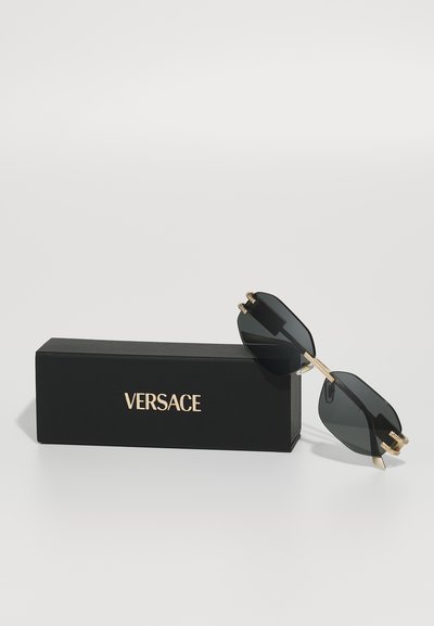 Crne sunčane naočale s oktagonalnim lećama, zlatnim detaljima i crnom kutijom koja prikazuje "VERSACE" u zlatnom slovu.