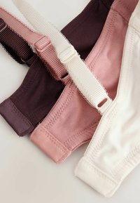 Trois soutiens-gorge en tissu doux en violet foncé, rose poussiéreux et blanc cassé, montrant des bretelles réglables et des détails de couture.