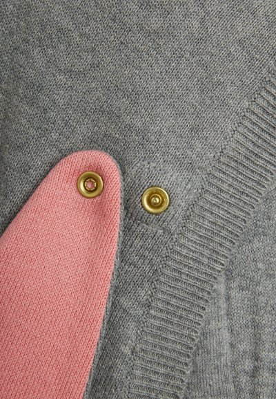 Gros plan sur un tissu tricoté gris et rose relié par deux boutons-pression dorés sur un vêtement.
