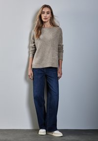 Beige stickad tröja med ribbat mönster och långa ärmar, tillsammans med mörkblå vida jeans och ljusa sneakers.