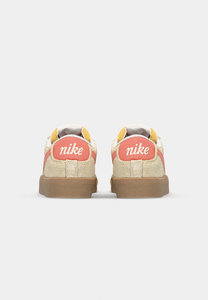 Baskets Nike avec une tige en daim beige, des accents roses et jaunes, une doublure blanche et une semelle en caoutchouc marron. Marque visible sur les talons.