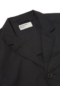 Giacca nera con colletto a scialle, bottone singolo e etichetta del marchio "Universal Works". Tessuto liscio con una sottile trama.