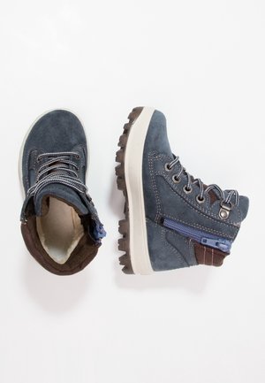 Paire de bottes d'enfant en daim bleu avec semelles blanches, lacets, fermeture éclair latérale et col marron rembourré sur fond blanc.