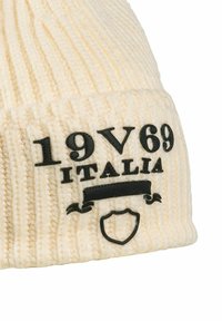 Cream knit beanie with black text "19V69 ITALIA" and a shield emblem. Features a textured ribbed design and a fold-up cuff.
