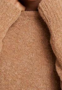 Maglione marrone lavorato a maglia con una texture morbida e pelosa e ampi polsini. Presenta un collo alto e un aspetto accogliente.