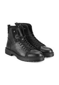 Bottines en cuir noir avec finition texturée, semelles en caoutchouc, lacets à l'avant et détail de fermeture éclair sur le côté. Présente des accents en daim et du matériel en métal.