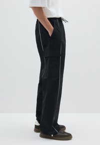 Zwarte cargobroek met contrasterende witte zijnaden, voorzien van een elastische tailleband en zijzakken, gemaakt van lichtgewicht stof.