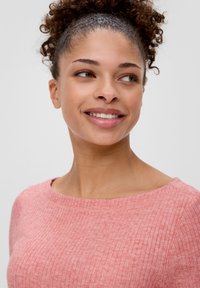 Helles pinkes, geripptes Sweatshirt mit weitem Ausschnitt, weicher Textur und figurbetontem Design, getragen von einer Person mit lockigem Haar.