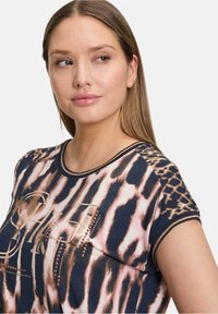 Kék, rövid ujjú felső rózsaszín leopárdmintával és csíkos mintákkal. Kerek nyakkivágással és fényes felületű díszgyöngyökkel rendelkezik.