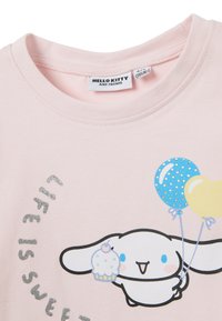 Roze katoenen t-shirt met een cartoonfiguur die een cupcake en ballonnen vasthoudt. Tekst "Life is sweet" in zilveren glitter, ronde halsontwerp.