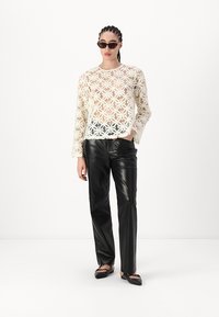 Haut en dentelle florale blanche avec des manches longues, associé à des pantalons en cuir noirs. Les accessoires comprennent des lunettes de soleil foncées et des chaussures plates noires.