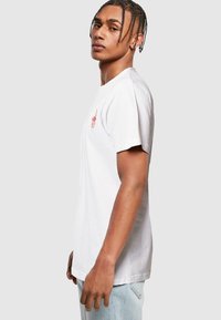 T-shirt en coton blanc à manches courtes, avec un petit design graphique rouge sur la poitrine, coupe décontractée et col rond.