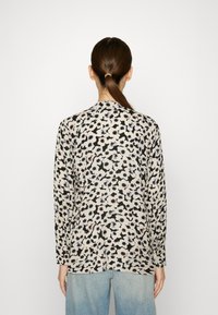 Top a maniche lunghe in tessuto leggero con un motivo maculato nero e beige. Collo rotondo e vestibilità comoda, abbinato a jeans azzurri.