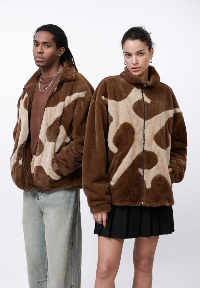 Bruine fleece jassen met een tan dierenprint; ritssluiting, hoge kraag, zijzakken. Model is gecombineerd met denim en een geplooide rok.