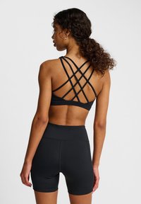 Svart sport-bh med korskraftiga remmar på baksidan, tillsammans med svarta högmidjade shorts. Har en slät och mjuk struktur.