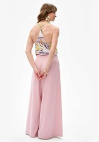 Mouwloze top met bloemenpatroon en een keyhole achterkant, gecombineerd met wijde roze broeken. Beschikt over delicate accessoires. Glad textuur.