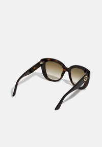 Gafas de sol carey con forma de ojo de gato, lentes degradados y acentos de hardware dorado en las patillas. Textura de plástico suave.