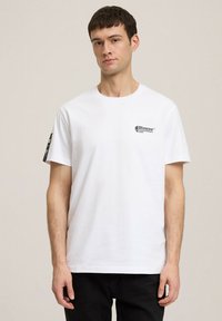 Biała bawełniana koszulka z krótkim rękawem, z czarnym logo na lewej piersi i kontrastową grafiką na prawym rękawie.