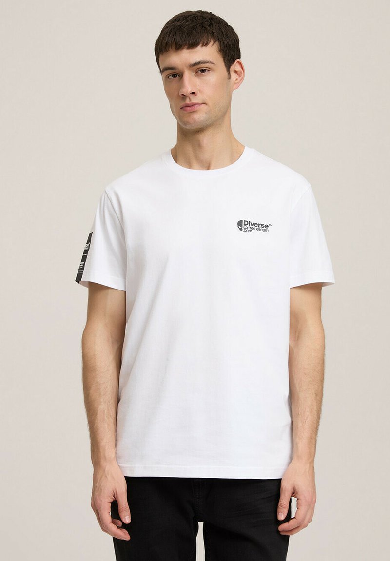 Biała bawełniana koszulka z krótkim rękawem, z czarnym logo na lewej piersi i kontrastową grafiką na prawym rękawie.