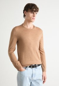 Light brown, long-sleeve, crew-neck sweater made of soft fabric. Paired with light blue denim jeans and a black belt.