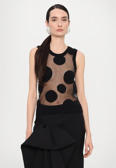 Black sleeveless top with a sheer fabric featuring large black polka dots, ribbed neckline, and paired with a black skirt with a bow detail.