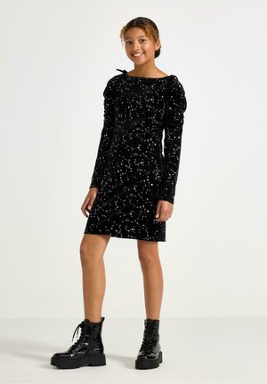 Černé sametové šaty s dlouhými rukávy, přiléhavým střihem a hvězdným vzorem. Doplněné černými platformovými botami na šněrování.