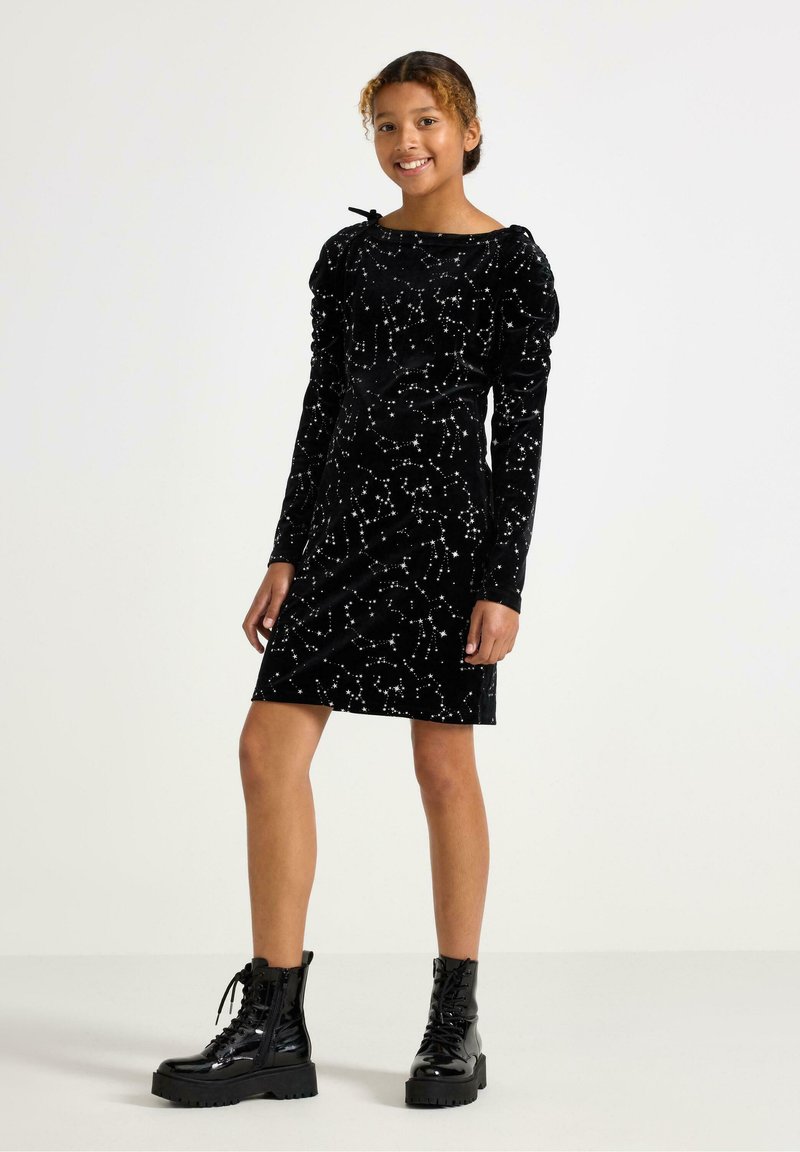 Sort velourkjole med lange ærmer, en tætsiddende pasform og et stjerneskyet mønster. Kombineret med sorte snørebåndsplatformstøvler.