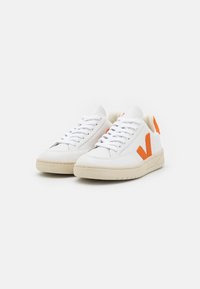 Baskets en cuir blanc avec des accents orange, caractérisées par une texture lisse, un bout rond et un design minimaliste avec un système de laçage.