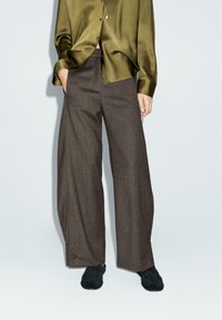 Pantaloni marroni a gamba larga realizzati in tessuto testurizzato, con vita alta e tasche laterali, abbinati a una camicia botton-up in satin verde.
