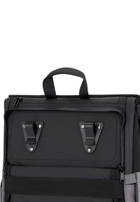 Svart ryggsäck med en hållbar tygutsida, övre handtag, två spännen och ett blixtlåsfack. Har en grå accent på sidan.