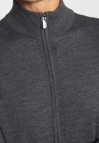 Grå zip-up tröja med hög krage, tillverkad av ett mjukt, strukturerat tyg. Har detaljer med en kontrasterande dragkedja framtill.