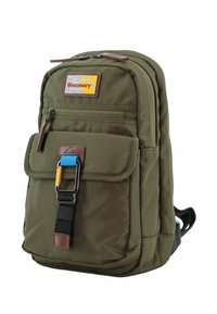 Zaino verde oliva in tessuto texturizzato, con molteplici tasche con cerniera, un risvolto anteriore e un accento blu su una tracolla nera. Presenta un'etichetta con logo.