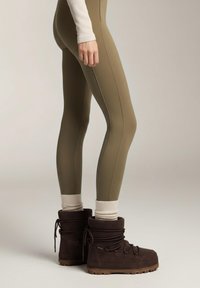 Legginsy w oliwkowym zielonym kolorze w połączeniu z brązowymi, sznurowanymi zimowymi butami. Buty mają prążkowany kołnierz i teksturowaną gumową podeszwę.