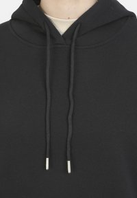 Sudadera negra hecha de tejido suave, con un bolsillo frontal y cordones con puntas de plata; diseño minimalista y superficie texturizada.