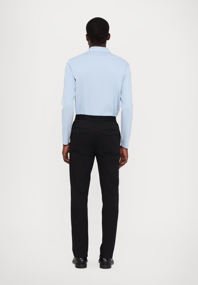 Camisa de manga larga azul claro con cuello, combinada con pantalones negros que tienen una cintura elástica y dos bolsillos traseros.