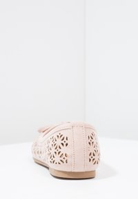 Růžová semišová obuv s výřezovým květinovým vzorem, plochou podrážkou, dekoračním mašlí na vrchu a prošívanými detaily na patě a po stranách.