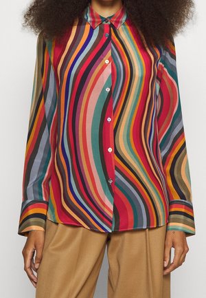 Langärmliges, mehrfarbig wellenförmig gestreiftes Hemd zum Knöpfen, getragen mit beigefarbenen Hosen, gezeigt vom Hals bis zur Mitte des Oberschenkels.