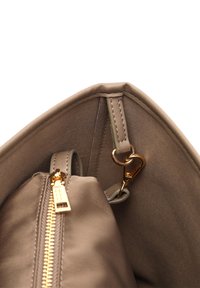 Unutrašnjost bež torbe od tkanine, s zlatnim zatvaračem, kopčom za ključeve i glatkom podstavom s lagano teksturiranom površinom.