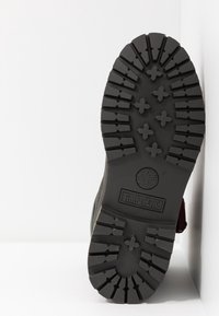 Semelle d'une chaussure Timberland noire avec des crampons profonds et des formes croisées surélevées pour l'adhérence, avec le logo et le nom de la marque embossés au centre de la semelle.