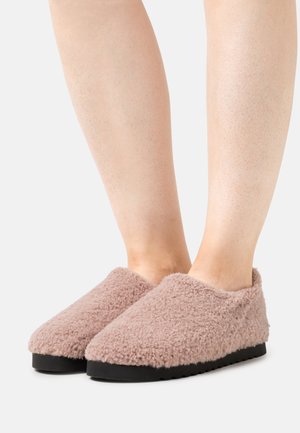 Fuzzy, pink slippers with a soft texture, rounded design, and a black, textured sole, featuring an open back for easy wear.