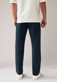 Marineblauwe broek met een rechte snit, gemaakt van lichtgewicht materiaal, gecombineerd met witte sneakers. Heeft een gladde textuur en geen zichtbare patronen.
