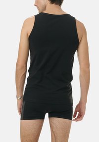 Black, sleeveless tank top made of smooth fabric, featuring a round neckline and a relaxed fit. Worn with black underwear, viewed from the back.