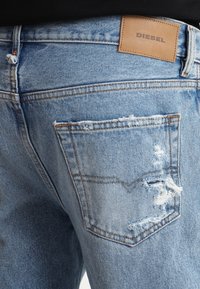 Ljusblå denimjeans med en sliten design och fransade kanter. Inkluderar en läderetikett märkt "DIESEL" på midjebandet och en bakficka.