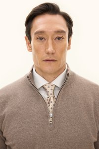 Maglione brown con zip e collo alto sopra una camicia azzurro chiaro, abbinato a una cravatta beige con motivi floreali blu e marroni. Tessuto morbido, vestibilità classica.