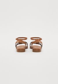 Sandales en cuir marron avec un design à lanières, une ouverture à l'arrière et une semelle plate, dotées d'une lanière de cheville réglable. Texture lisse avec des accents minimaux.