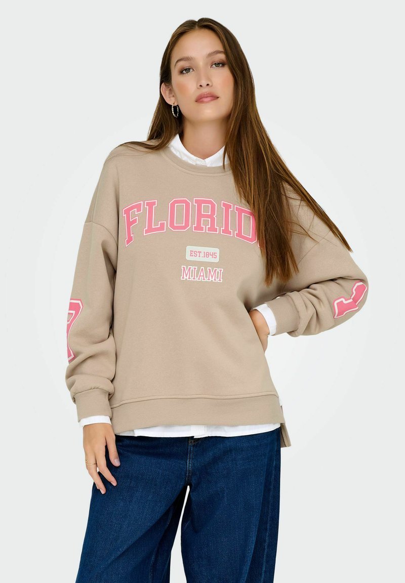 Sweat-shirt beige avec "FLORIDA" et "MIAMI" imprimés en rose. Design décontracté avec des poignets et un ourlet côtelés, superposé à une chemise blanche.